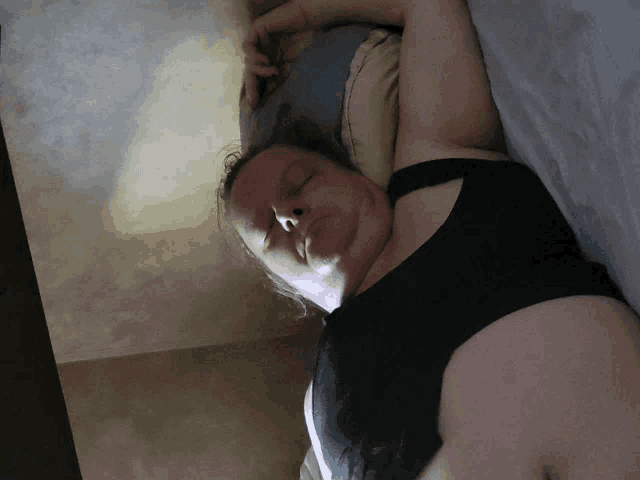 a woman in a black tank top is laying on a bed with her eyes closed