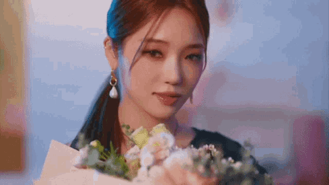 a woman is holding a bouquet of flowers in her hands and looking at the camera .