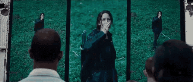 a group of people are watching a video of a woman covering her mouth while standing in a field .