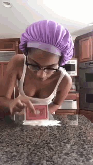 a woman wearing a purple hat and glasses is standing on a counter .