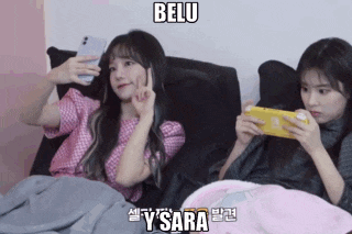 two girls are laying on a couch and one is holding a phone and the other is holding a video game controller
