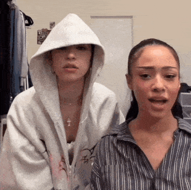 two women standing next to each other with one wearing a hoodie with a cross on it