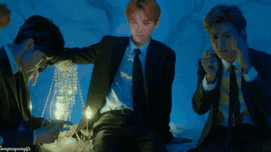a group of men in suits and ties are sitting around a chandelier