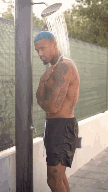 a shirtless man with blue hair is taking a shower with a shower head