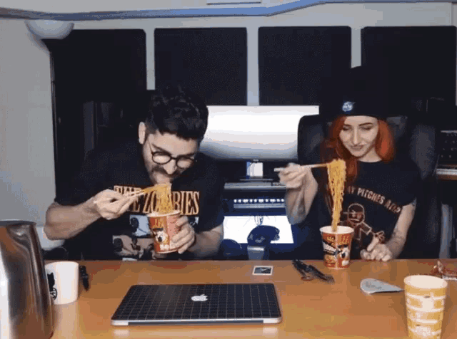 a man and a woman are eating noodles with chopsticks while wearing zombies shirts
