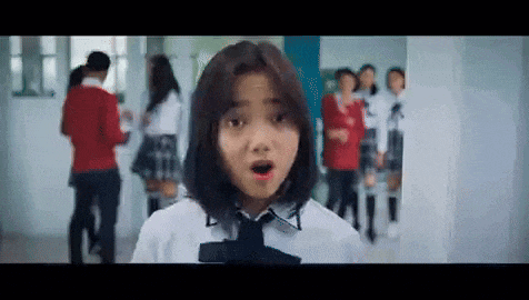 a girl in a school uniform and tie is standing in a hallway with a surprised look on her face .
