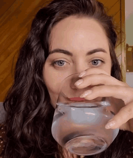 a woman drinking a glass of water from a bowl