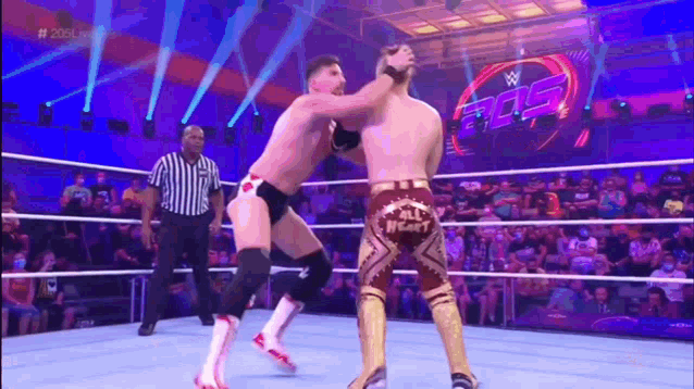 two men are wrestling in a wrestling ring while a referee looks on .