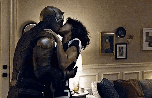 a man in a superhero costume and a woman are kissing in a living room .