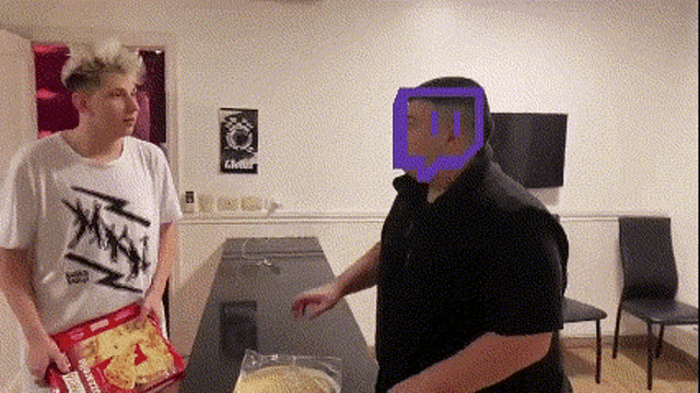 two men are standing next to each other in a room with a box of doritos in front of them .
