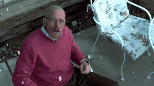 a man in a pink sweater and glasses is sitting in a chair on a patio .