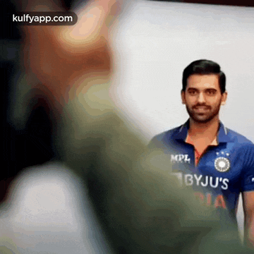 a man in a blue shirt with the word bbyju 's on it is standing in front of a white wall .