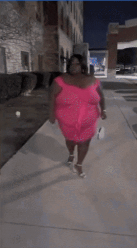 a woman in a pink dress stands on a sidewalk
