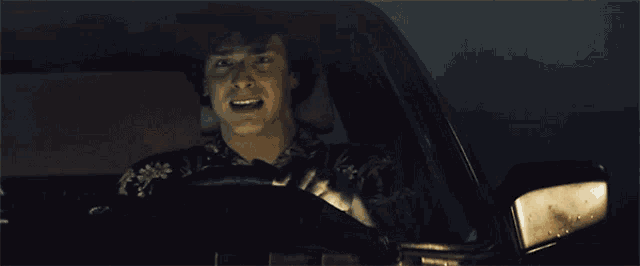 a person sitting in a car with a reflection of another person in the mirror
