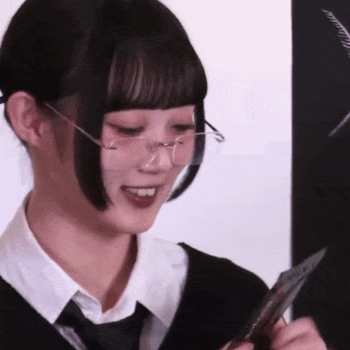 a girl wearing glasses and a tie is smiling while holding a piece of paper .