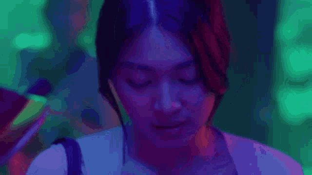 a close up of a woman 's face in a dark room with purple and blue lights .