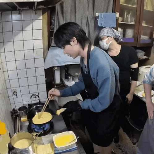 a man wearing a mask is cooking in a kitchen with other people