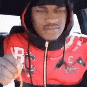 a man in a red hoodie is holding a french fry in his hand .