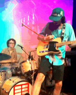 a man is playing a guitar in front of a drum set and a microphone