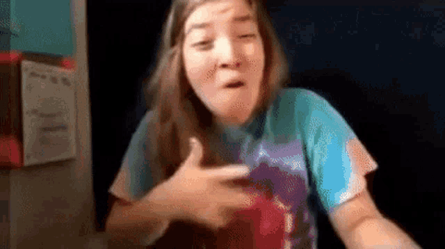 a girl in a tie dye shirt is pointing at her chest .