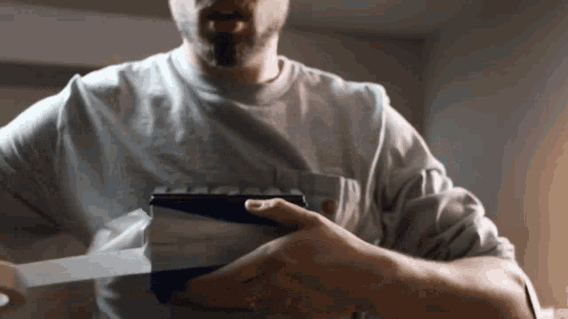 a man in a grey shirt is holding a blue and white object in his hands