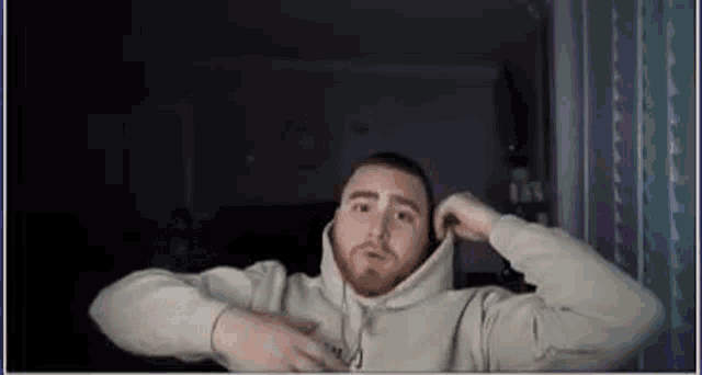 a man with a beard is wearing a hoodie and headphones while sitting in front of a window .