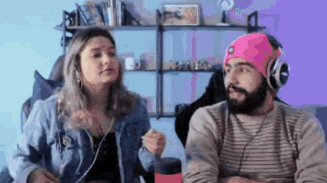 a man and a woman are sitting next to each other wearing headphones and a pink hat .