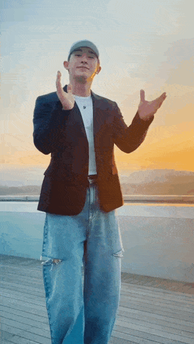 a man wearing a hat and a jacket is standing on a balcony with his hands in the air .
