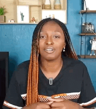 a woman with braids is making a funny face while sitting in front of a shelf .