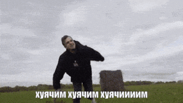 a man in a black sweatshirt is standing in a field with a bale of hay in the background