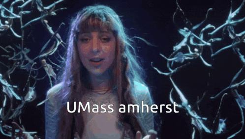 a woman with long hair says umass amherst in a dark room