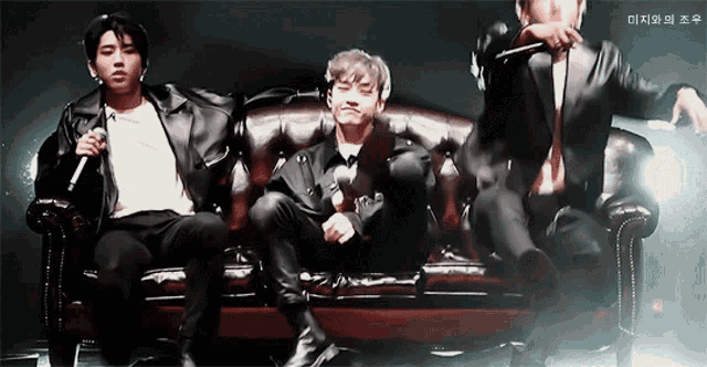 three men are sitting on a couch and one has a microphone