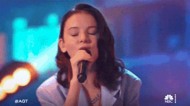 a young woman is singing into a microphone with her eyes closed .