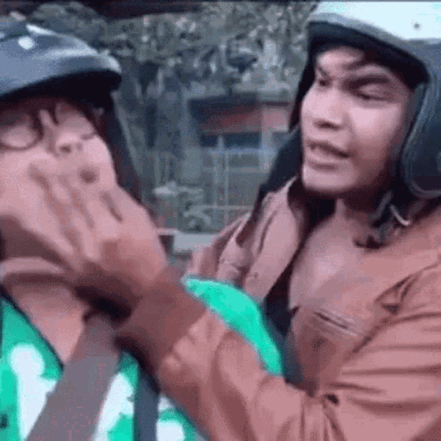 a man is putting a helmet on another man 's head while sitting in a car .