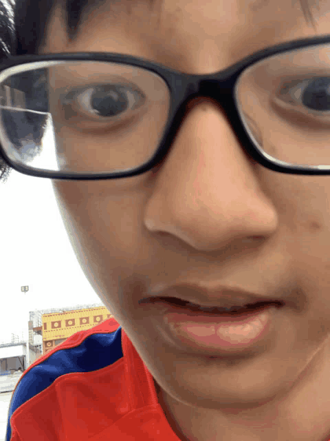 a close up of a person 's face with glasses and a red and blue shirt