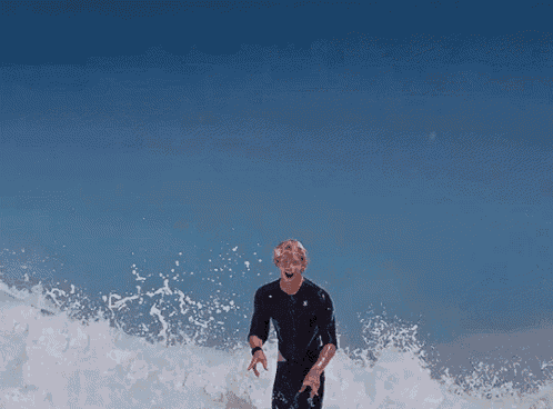 a man in a black wetsuit is standing in the ocean