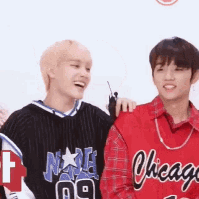 two young men are standing next to each other and laughing . one of the men is wearing a red chicago jersey .