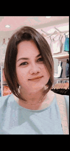 a woman wearing a light blue shirt is smiling in front of a rack of clothes