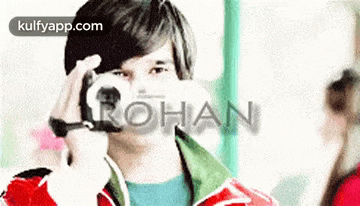 a young man is taking a picture with a camera and the word rohan is visible in the background .