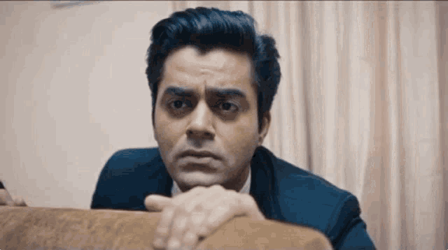a man in a suit and tie is leaning on a couch with his hand on his chin .