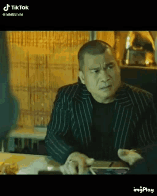 a man in a striped suit is sitting at a table with a cell phone .