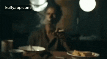 a man is sitting at a table smoking a cigarette .