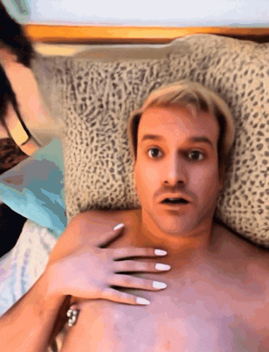 a shirtless man is laying on a bed with a woman holding his chest