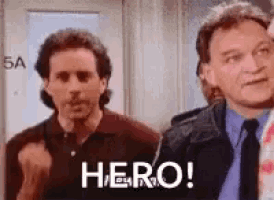 two men are standing next to each other in a room and one of them is giving a thumbs up .
