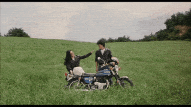 a man and a woman standing next to a blue honda motorcycle in a grassy field