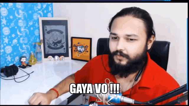 a man with a beard is sitting at a desk with a microphone and says gaya vo !!!