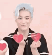 a young man with blue hair is holding a red heart in his hands .