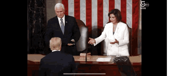 a man in a suit and tie is giving a speech in front of a woman in a white jacket
