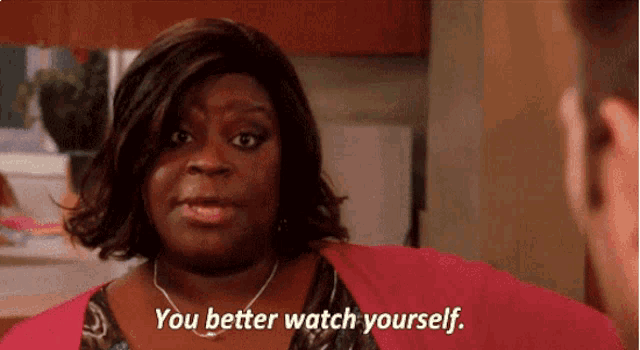 a woman in a pink shirt is talking to a man and says " you better watch yourself "