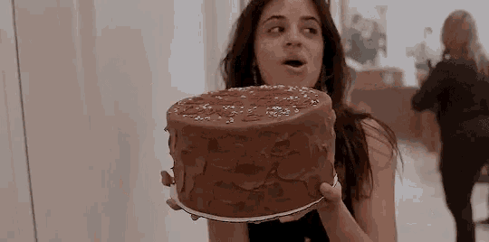 a woman is holding a chocolate cake with sprinkles on it .